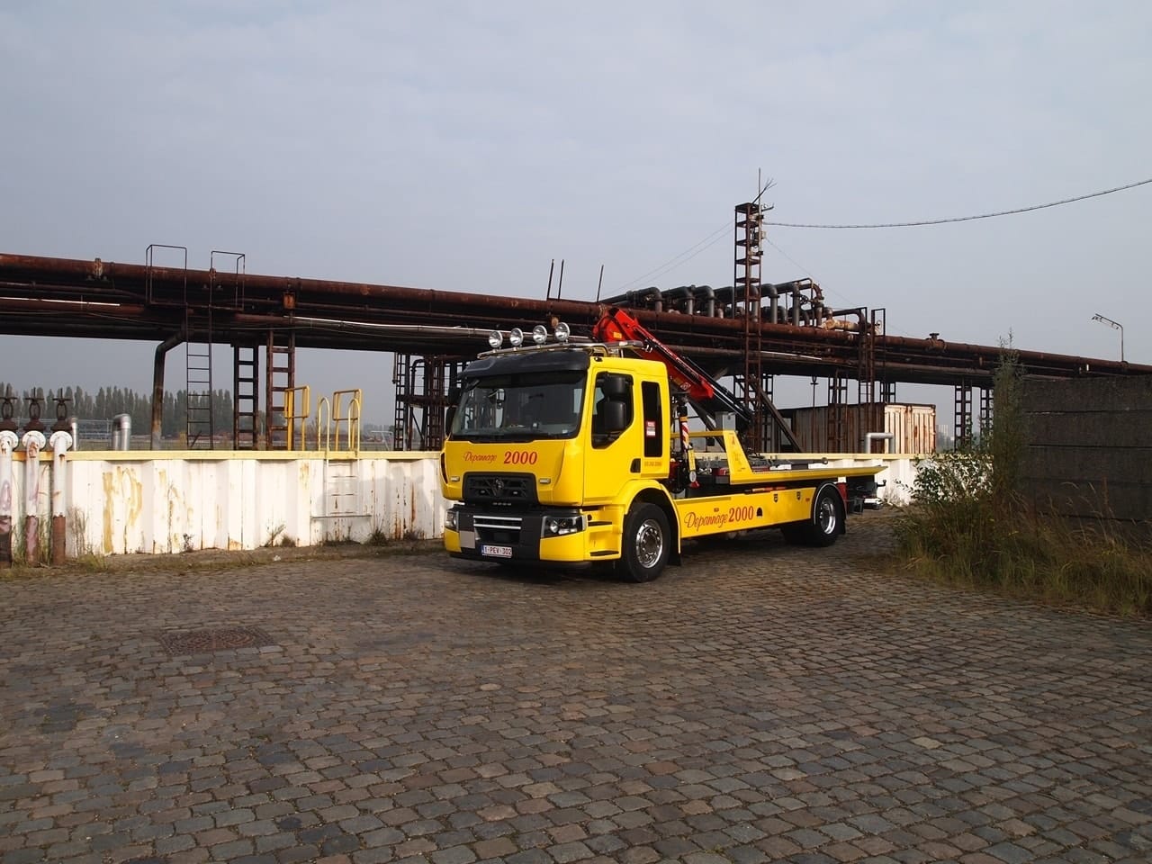 Twee gele takelwagens van Depannage 2000 met rode laadkranen naast elkaar op een terrein