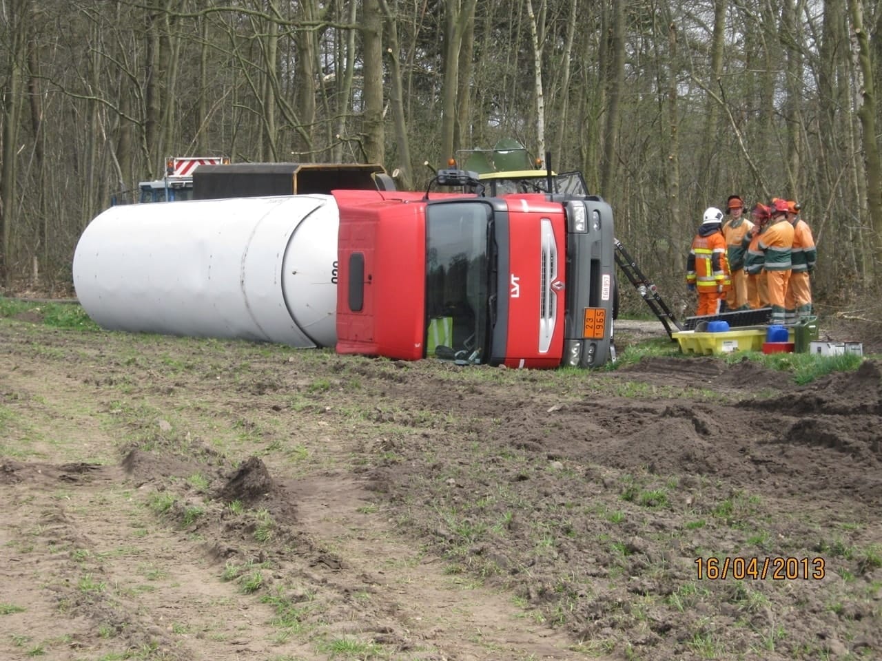 Op zijn kant liggende rood-witte tankvrachtwagen die geborgen wordt