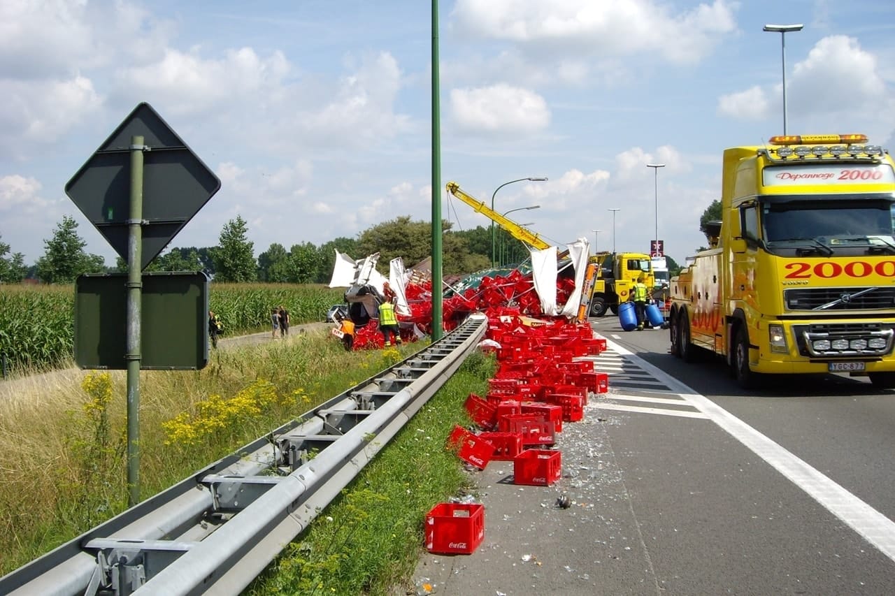 Geel voertuig van Depannage 2000 dat een wagen takelt langs een waterkade